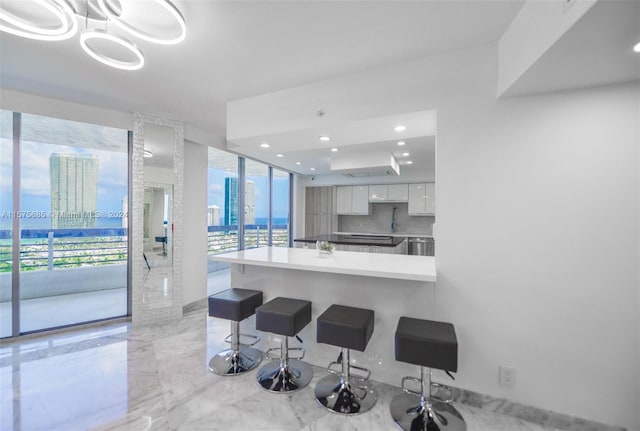 kitchen featuring backsplash, white cabinets, expansive windows, kitchen peninsula, and a breakfast bar