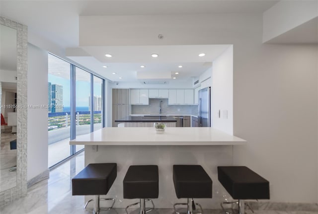 kitchen featuring white cabinets, kitchen peninsula, decorative backsplash, a kitchen breakfast bar, and stainless steel fridge