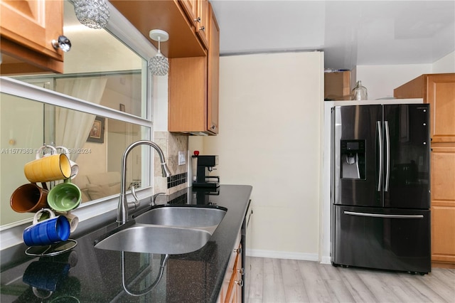 kitchen featuring pendant lighting, light wood-type flooring, black refrigerator with ice dispenser, sink, and tasteful backsplash