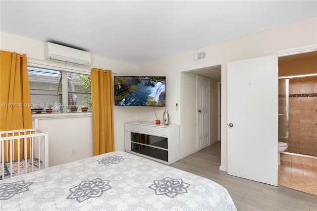 bedroom featuring an AC wall unit, light hardwood / wood-style floors, and connected bathroom