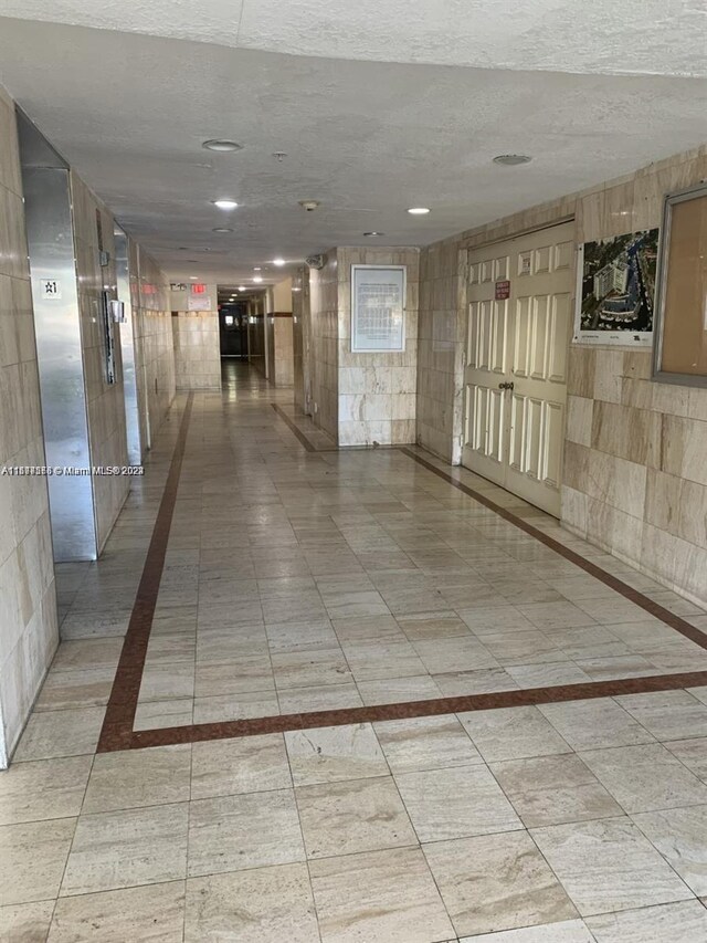 hall featuring tile walls, a textured ceiling, and light tile floors