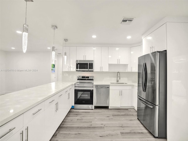 kitchen with decorative light fixtures, light hardwood / wood-style floors, appliances with stainless steel finishes, and white cabinetry