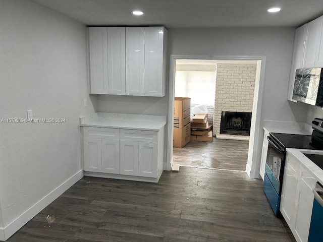 kitchen with dark wood-style floors, range with electric stovetop, stainless steel microwave, white cabinetry, and baseboards