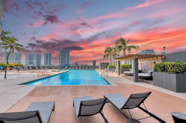 pool at dusk featuring a patio area and a pergola