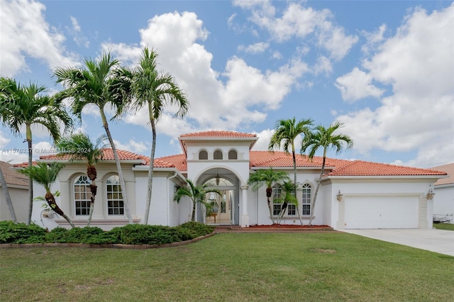 mediterranean / spanish home with a tile roof, stucco siding, a garage, driveway, and a front lawn