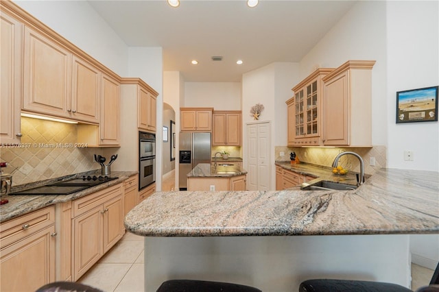 kitchen with light stone counters, appliances with stainless steel finishes, a kitchen breakfast bar, a peninsula, and a sink