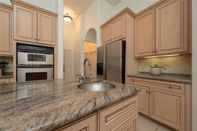 kitchen with light tile patterned floors, stainless steel appliances, sink, dark stone counters, and tasteful backsplash