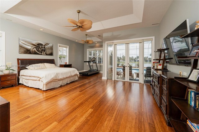 bedroom featuring a tray ceiling, light hardwood / wood-style flooring, access to exterior, and ceiling fan