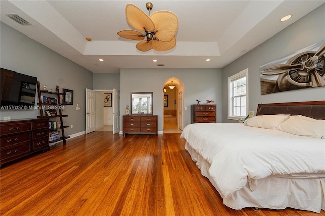 bedroom with arched walkways, recessed lighting, a raised ceiling, visible vents, and wood finished floors