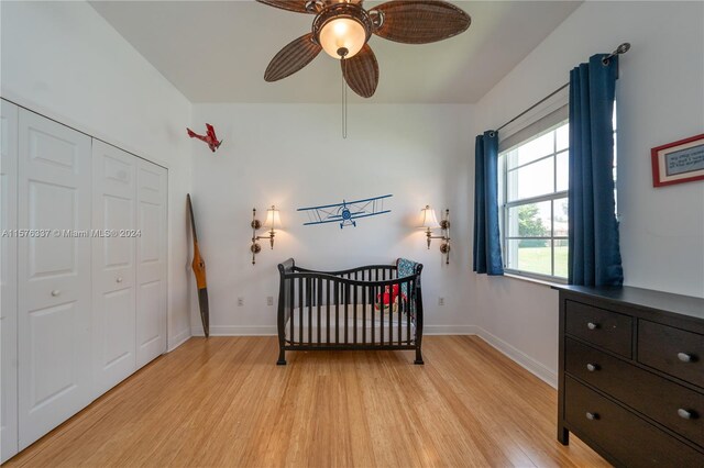 bedroom with a closet, a crib, ceiling fan, and light hardwood / wood-style floors