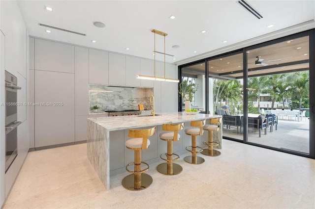 kitchen featuring decorative light fixtures, white cabinetry, backsplash, a wall of windows, and light stone counters