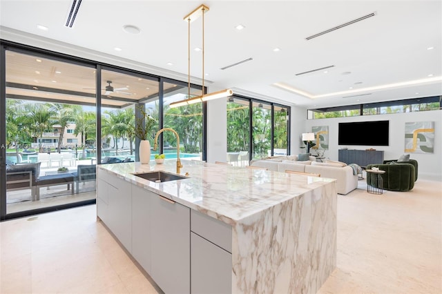 kitchen with sink, white cabinetry, floor to ceiling windows, light stone countertops, and an island with sink