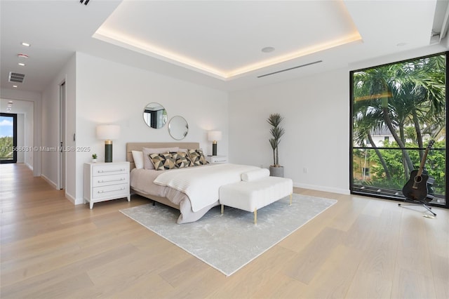 bedroom with floor to ceiling windows, a tray ceiling, and light hardwood / wood-style flooring