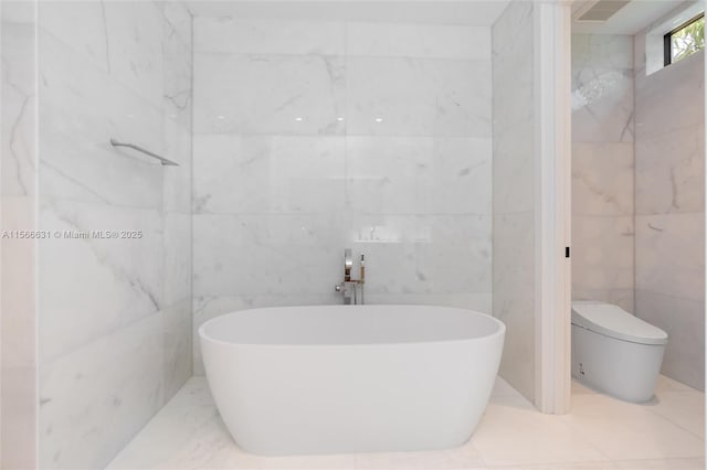 bathroom featuring a tub to relax in, toilet, and tile walls