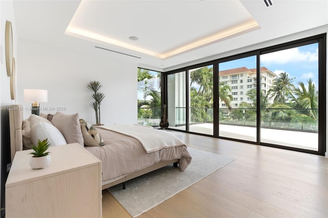 bedroom with floor to ceiling windows, a tray ceiling, access to exterior, and light hardwood / wood-style flooring