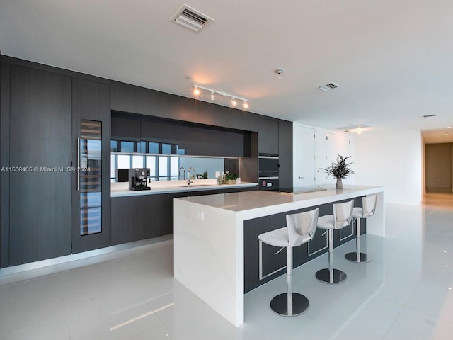 kitchen with sink, light tile flooring, rail lighting, and a kitchen island