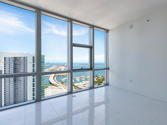 spare room featuring a wall of windows, a water view, and tile flooring