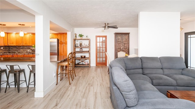 living room featuring ceiling fan, a textured ceiling, and light hardwood / wood-style flooring