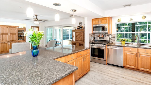 kitchen featuring sink, tasteful backsplash, decorative light fixtures, appliances with stainless steel finishes, and light hardwood / wood-style floors