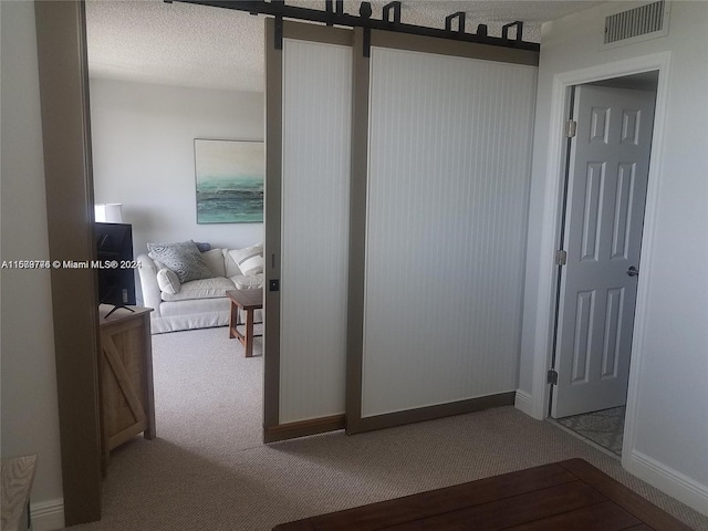 hallway with a textured ceiling, carpet, and a barn door