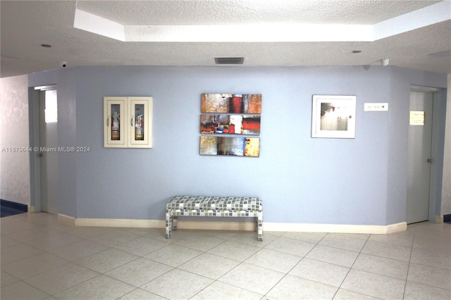 interior space featuring a textured ceiling, a tray ceiling, and light tile patterned floors