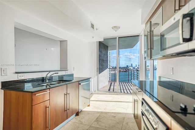 kitchen with dark stone countertops, a wall of windows, sink, and appliances with stainless steel finishes