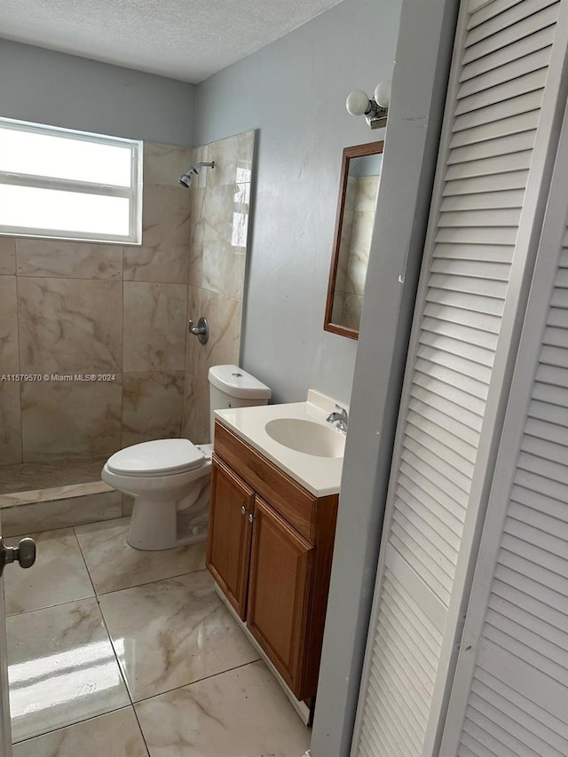 bathroom featuring vanity, tile flooring, a tile shower, toilet, and a textured ceiling