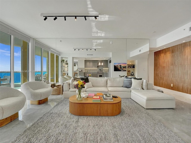 living room with a water view, light tile floors, rail lighting, floor to ceiling windows, and wood walls