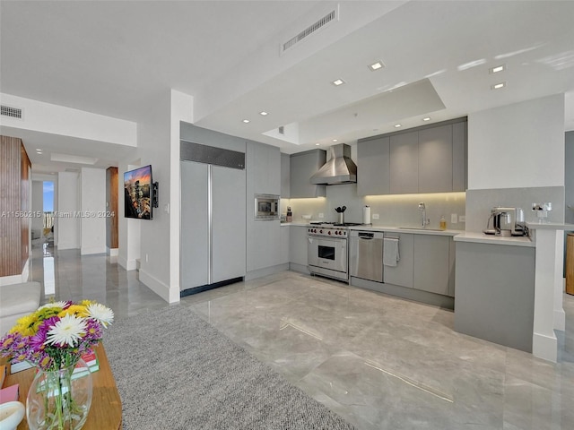 kitchen with built in appliances, light tile flooring, gray cabinets, wall chimney range hood, and a raised ceiling