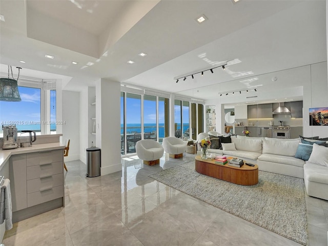 living room featuring rail lighting, light tile floors, a raised ceiling, and a water view