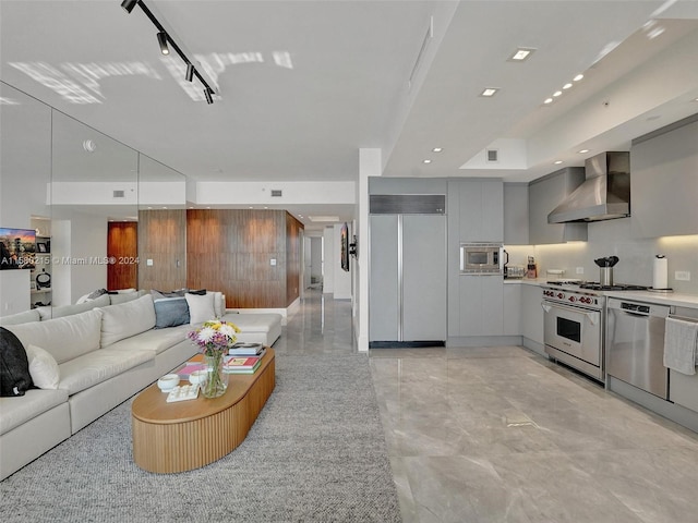 kitchen featuring built in appliances, gray cabinets, wall chimney range hood, light tile floors, and track lighting