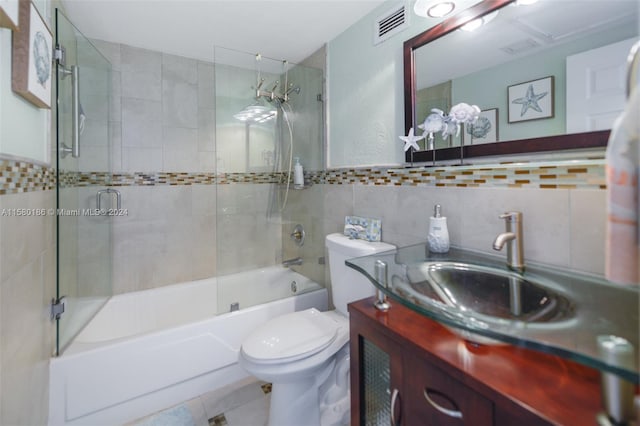 full bathroom featuring tile walls, bath / shower combo with glass door, large vanity, toilet, and tile flooring