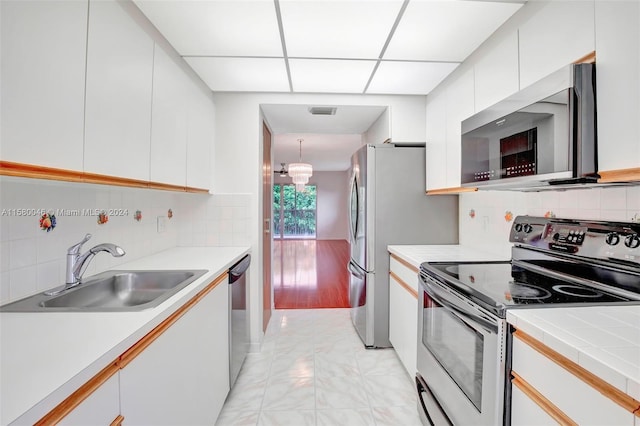 kitchen with tasteful backsplash, appliances with stainless steel finishes, light countertops, white cabinetry, and a sink