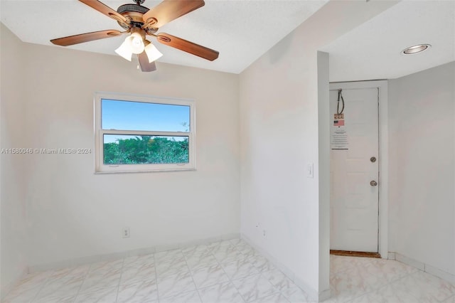 empty room with ceiling fan, marble finish floor, and baseboards