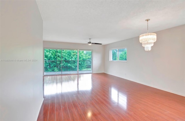 spare room featuring a textured ceiling, ceiling fan with notable chandelier, wood finished floors, and baseboards