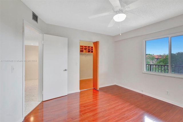 unfurnished bedroom with a closet, visible vents, a spacious closet, wood finished floors, and baseboards