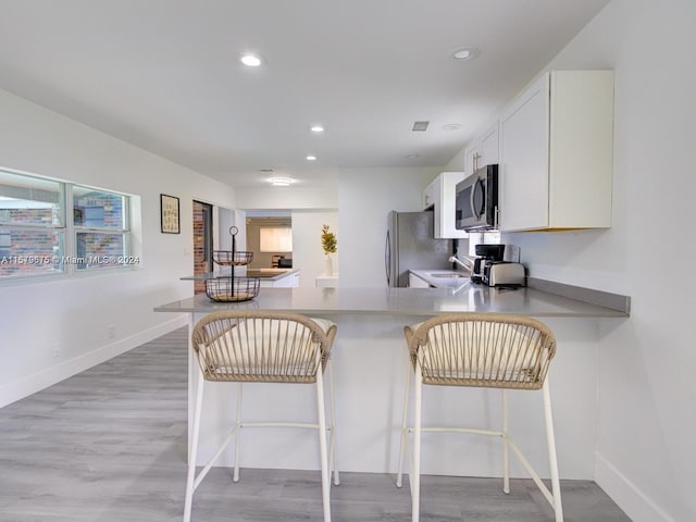 kitchen featuring kitchen peninsula, a kitchen bar, appliances with stainless steel finishes, light hardwood / wood-style floors, and white cabinetry