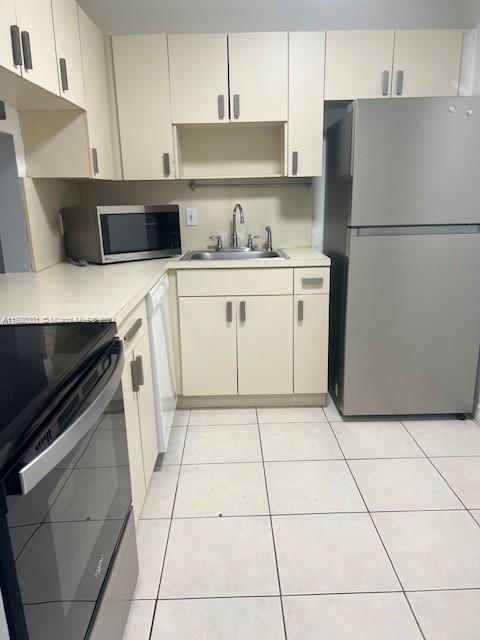 kitchen with sink, light tile patterned flooring, stainless steel appliances, and cream cabinetry