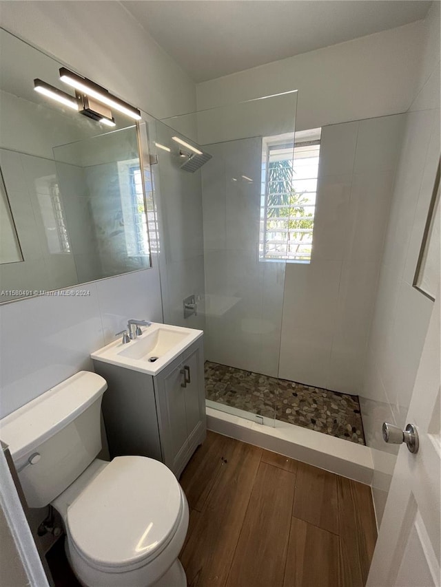 bathroom with wood-type flooring, tile walls, vanity, a tile shower, and toilet