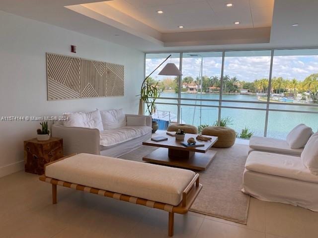 living room featuring plenty of natural light, a water view, tile flooring, and a tray ceiling