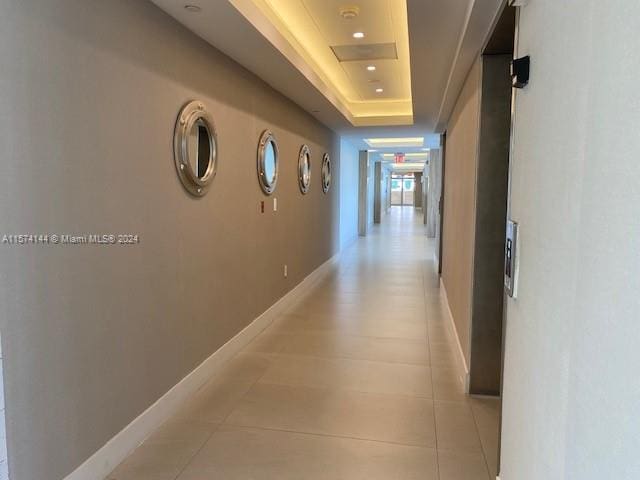 corridor with a raised ceiling and light tile floors