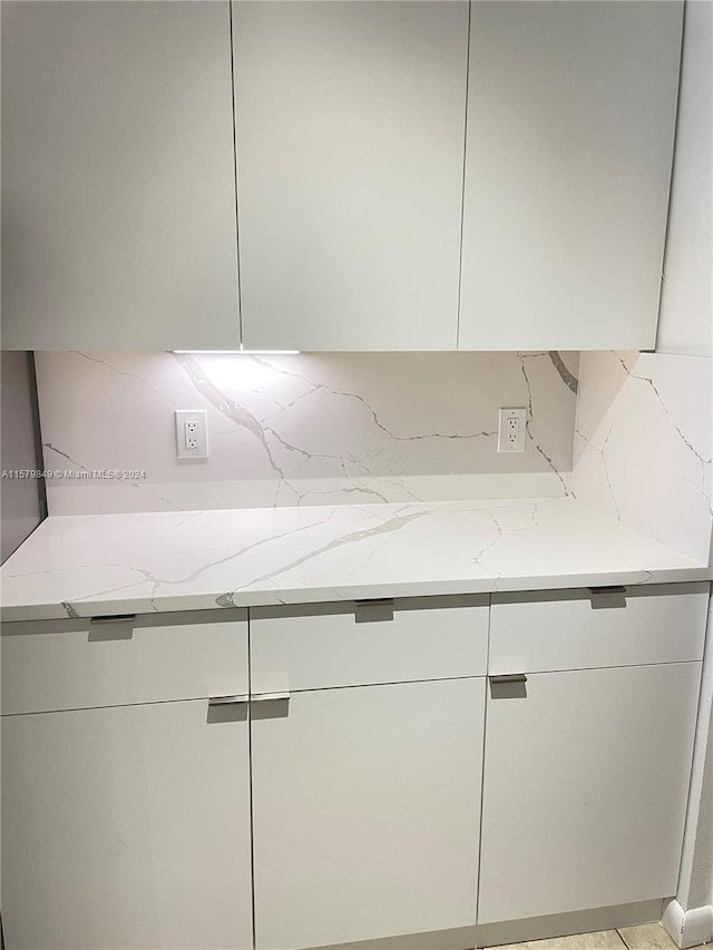 kitchen featuring backsplash, white cabinets, and light stone countertops