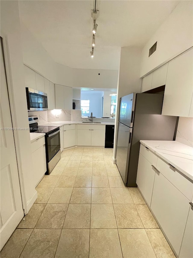 kitchen featuring appliances with stainless steel finishes, sink, light tile flooring, track lighting, and light stone countertops