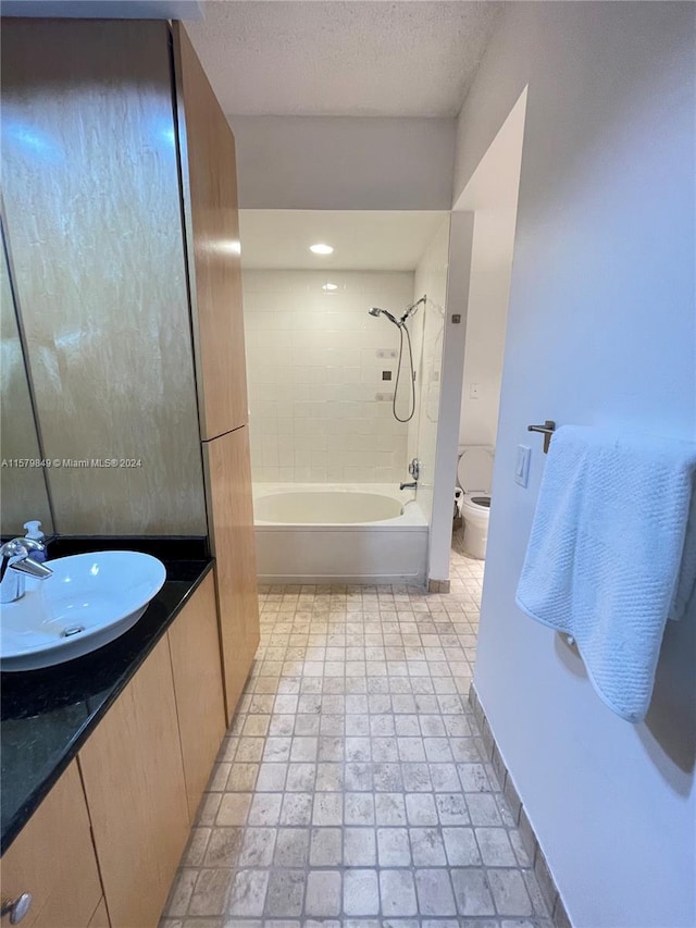 full bathroom with tile flooring, tiled shower / bath combo, a textured ceiling, toilet, and vanity