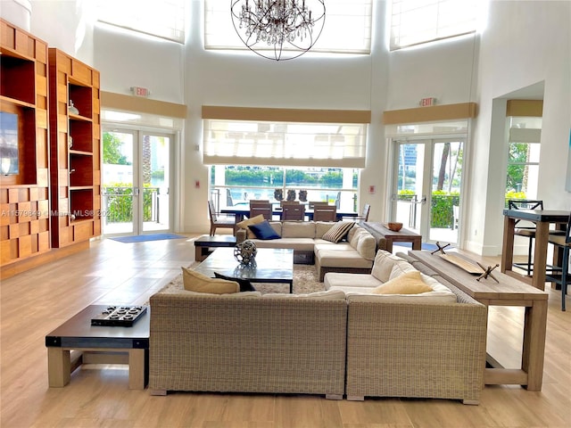 living room with french doors, a towering ceiling, light hardwood / wood-style floors, and a notable chandelier