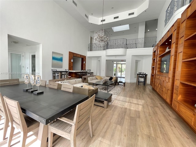 dining space with a skylight, a notable chandelier, a raised ceiling, a high ceiling, and light hardwood / wood-style flooring