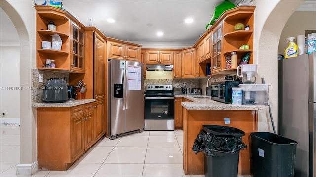 kitchen featuring stainless steel appliances, tasteful backsplash, light stone counters, sink, and light tile floors