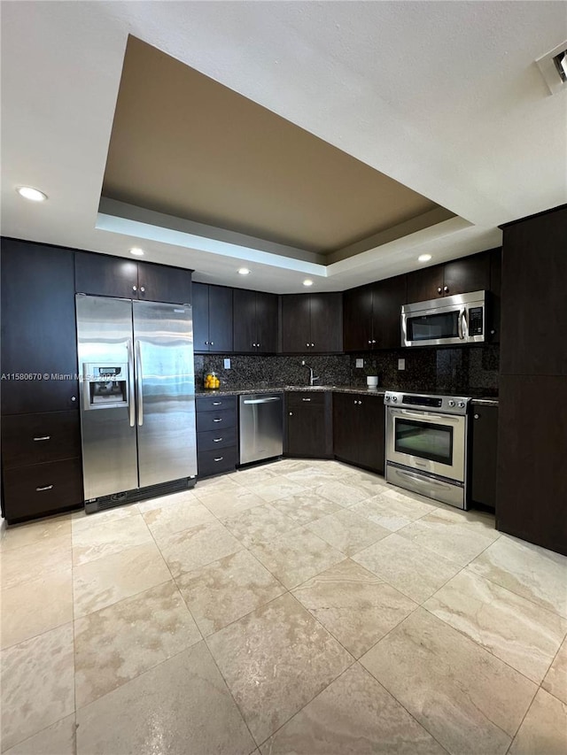 kitchen featuring stainless steel appliances, a tray ceiling, tasteful backsplash, sink, and light tile floors