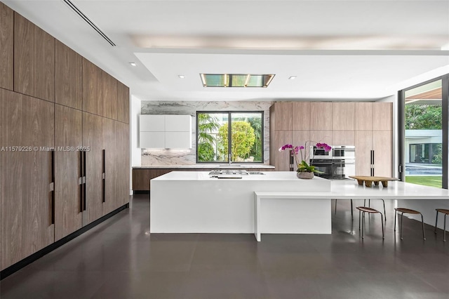kitchen with modern cabinets, a kitchen bar, backsplash, and a healthy amount of sunlight