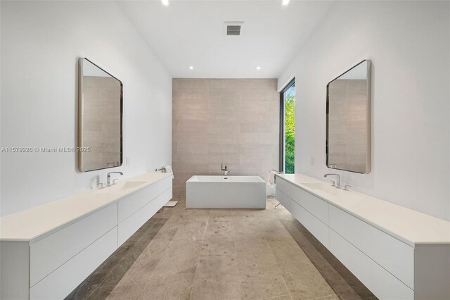 bathroom with a freestanding bath, two vanities, visible vents, and a sink